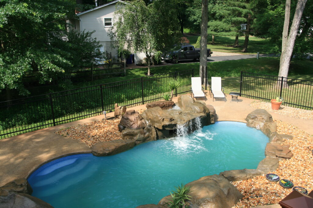 swimming pool with big Boulder coping stones small grotto and waterfall surrounded by trees